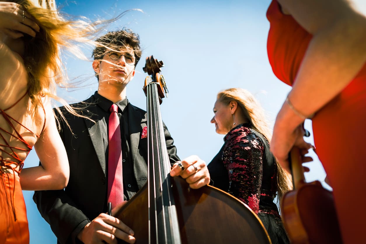Three musicians in red dress and one musician in black suit at the beach.