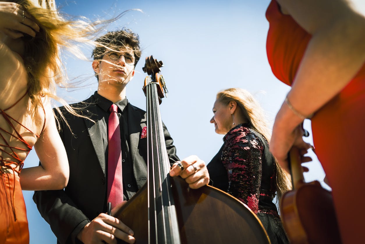 Three musicians in red dress and one musician in black suit at the beach.